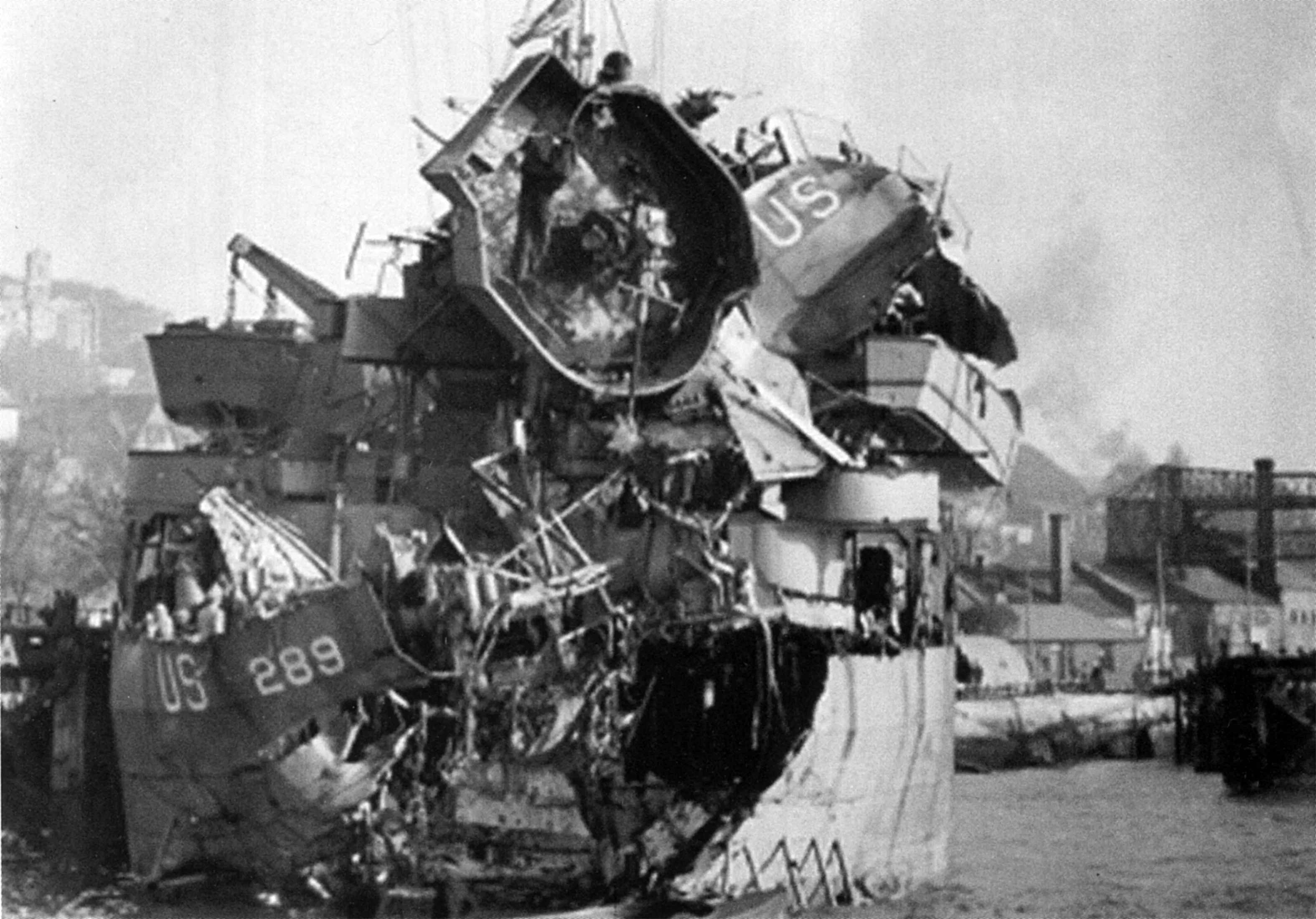 A photograph of LST-289 after the attack. The ship is almost wholly destroyed, with the bridge collapsed in on itself and the hull opened up on the stern.