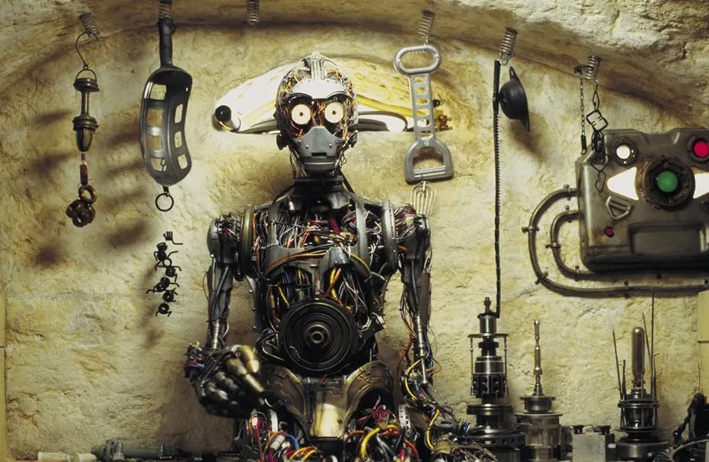 A still from The Phantom Menace showing C-3PO without any of his distinctive yellow plating, and instead only sporting a grey metallic skeleton with a large amount of vein like wires visible